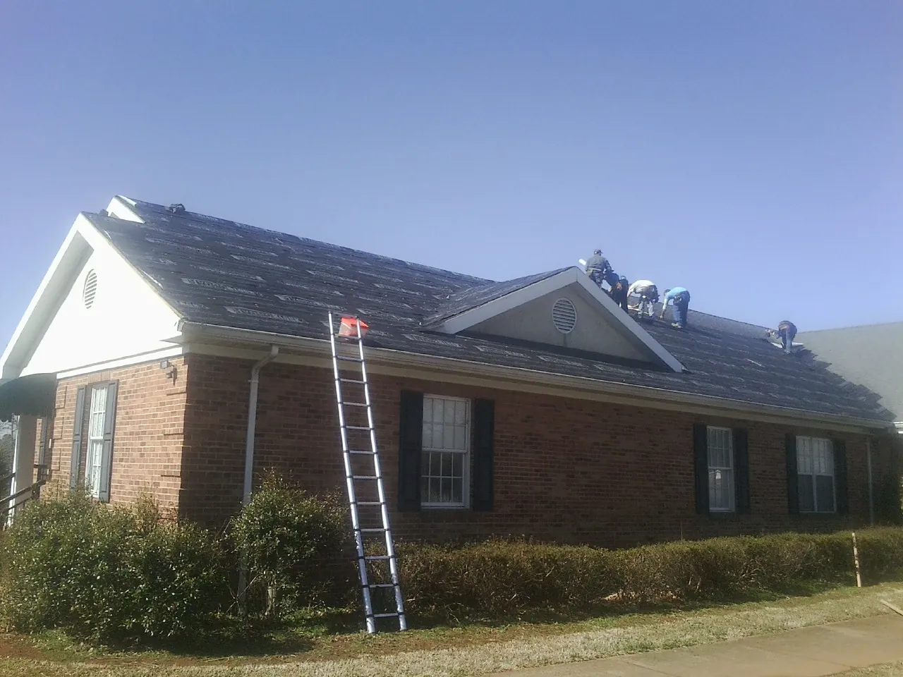 Crew tearing shingles off a brick ranch roof with a ladder set — Emergency Roof Repair work by our crew in Macomb