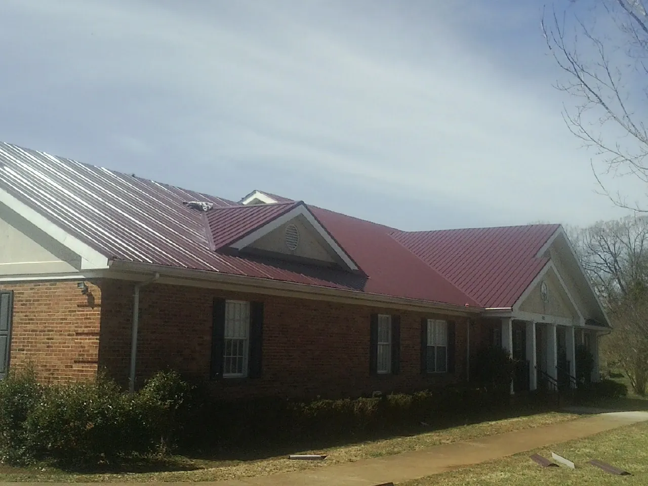 Red metal roof with gabled entries on a long brick building, from a Hail Damage Roof Repair job in Macomb